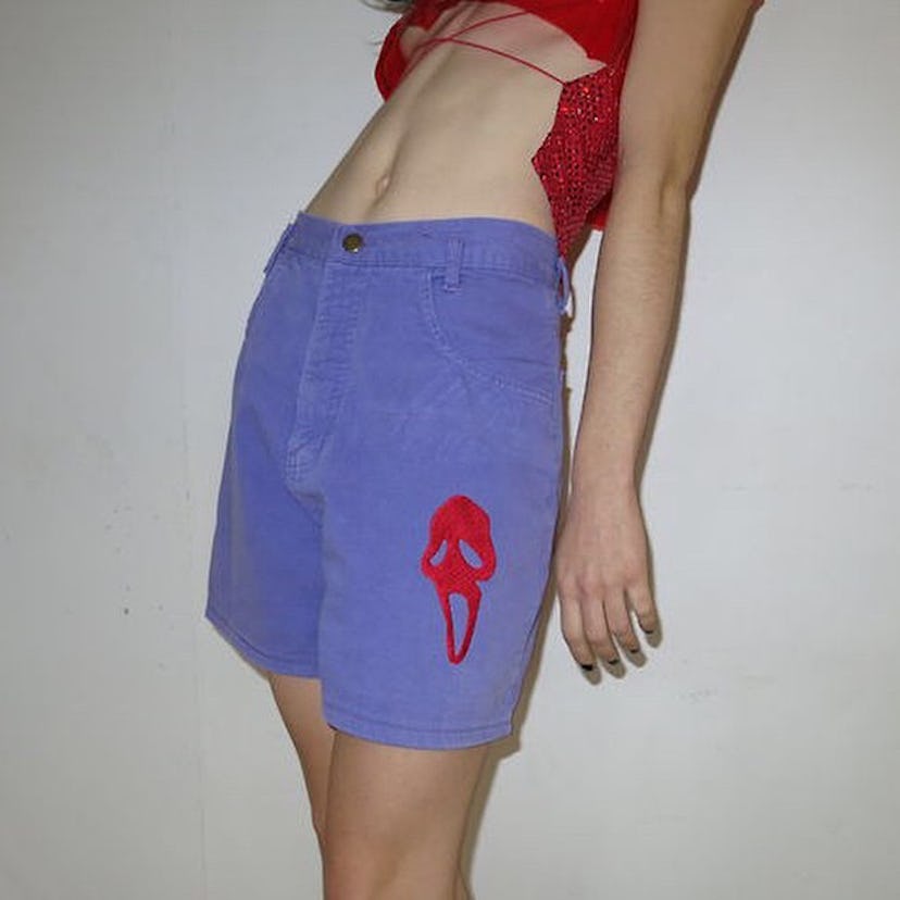 A woman wearing a red string top and blue shorts with the scream logo on them