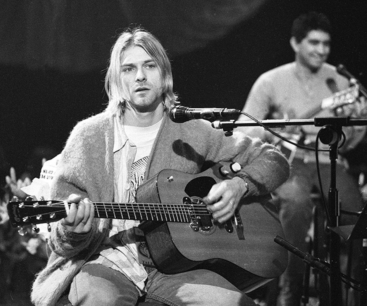 Kurt Cobain holding a guitar with a microphone in front of him in a black and white picture