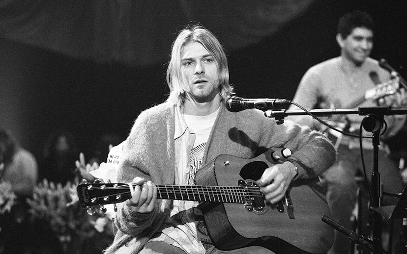 Kurt Cobain holding a guitar with a microphone in front of him in a black and white picture