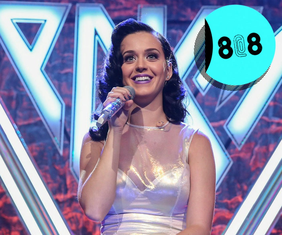 Smiling Katy Perry sitting in a sparkly dress while holding a microphone