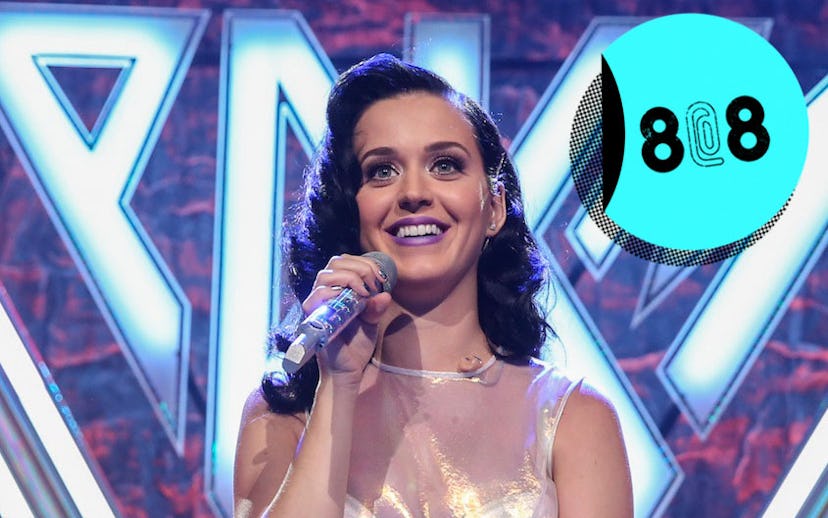 Smiling Katy Perry sitting in a sparkly dress while holding a microphone