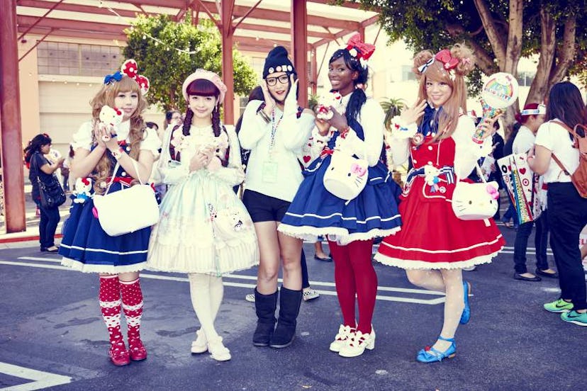 Five young girls dressed in Hello Kitty costumes while holding same bags in the shape of Hello Kitty...