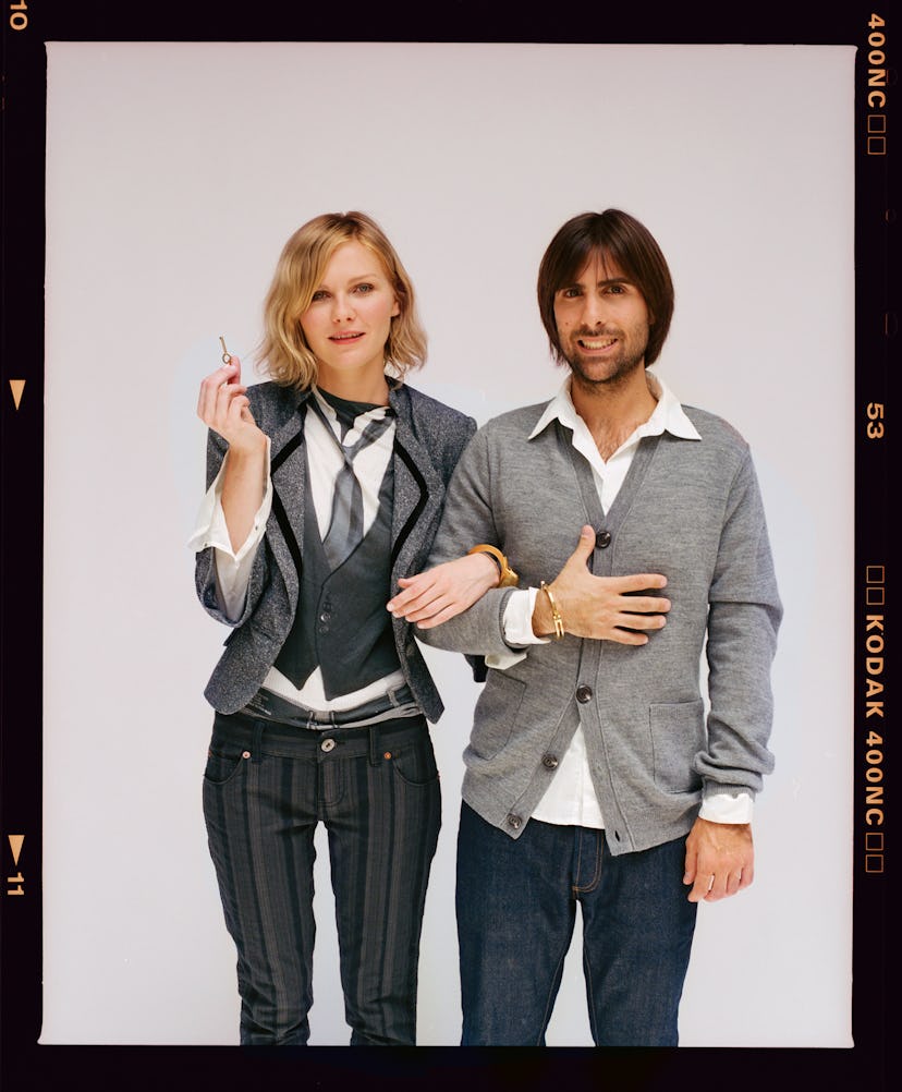Jason Schwartzman in a gray jacket and Kirsten Dunst in a gray suit with their arms entangled