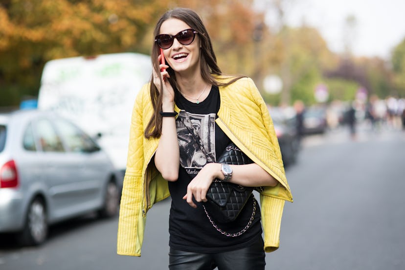 A brunette talking on her phone and wearing a black shirt and yellow jacket