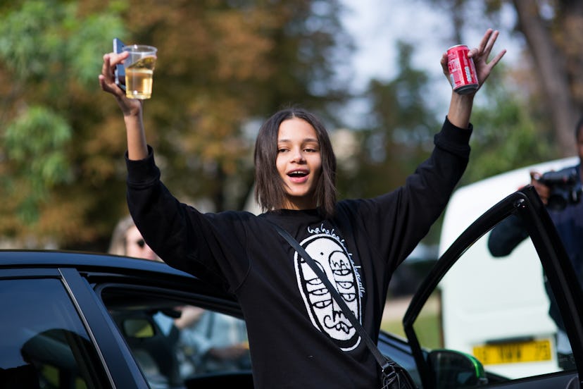 Street style dressed girl holding a can of coke and plastic glass with wine
