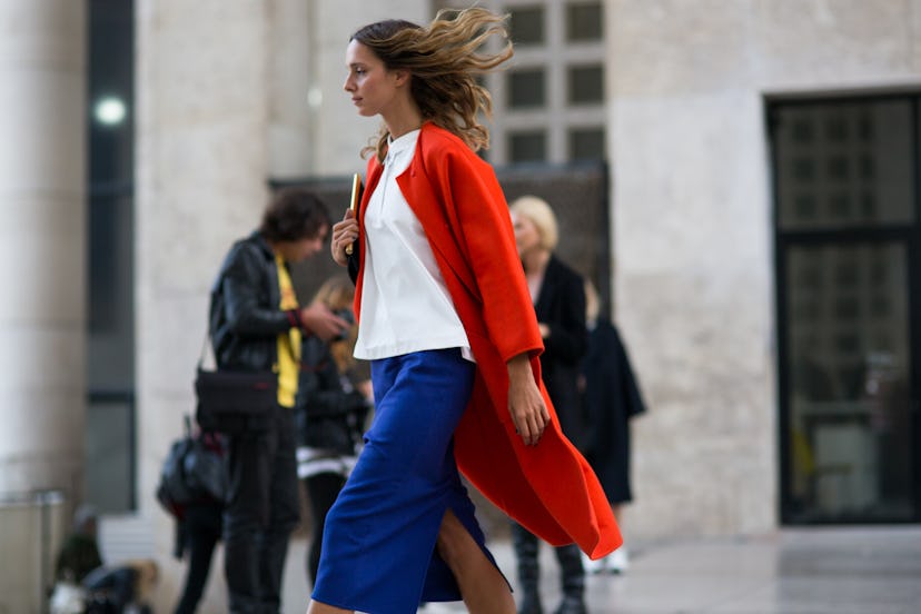 Young lady walking in a red coat and blue skirt down the streets of Paris