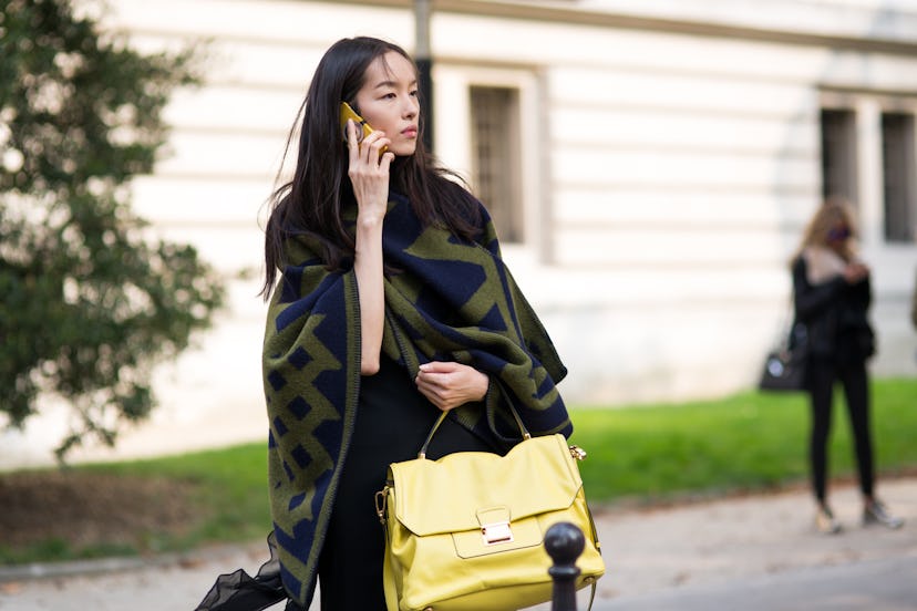 A lady with a yellow handbag and green and black coat talks on her phone