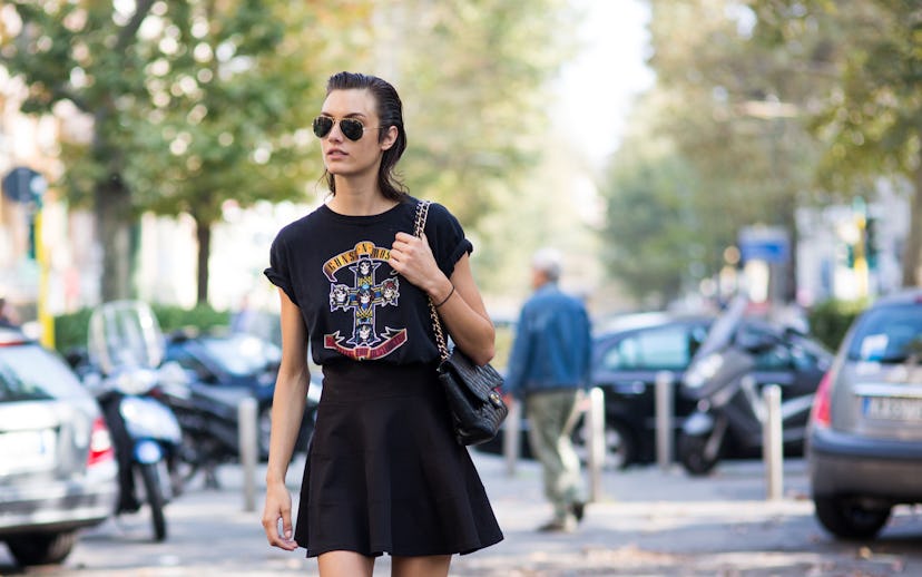 A model in a black t-shirt and black skirt walking on the street