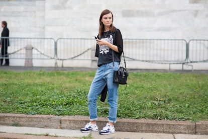 A Brunette woman in a fall combination of a black shirt and blue denim pants, black bag and white an...