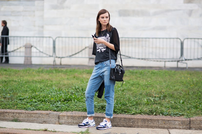 A Brunette woman in a fall combination of a black shirt and blue denim pants, black bag and white an...