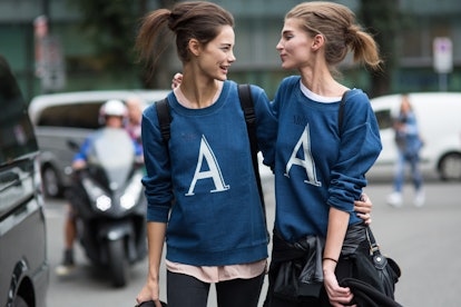 Two female friends in blue sweaters with big "A" letter signs facing each other with the same up-do ...