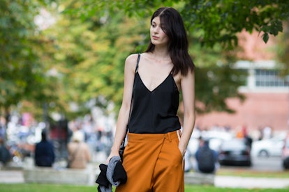 A black-haired lady in a black v-neck top and orange pants