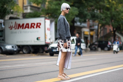 A woman in a grey sweater, short geometric print dress and tan shoes holding a shopping bag