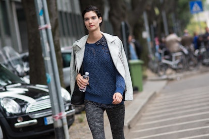 A black-haired woman walking in a blue sweater and white jacket down the streets of Milan