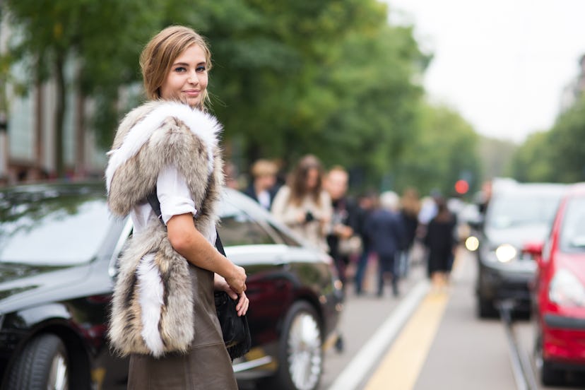A woman looking over her right shoulder in a white mid-length sleeved shirt, brown and white fur ves...