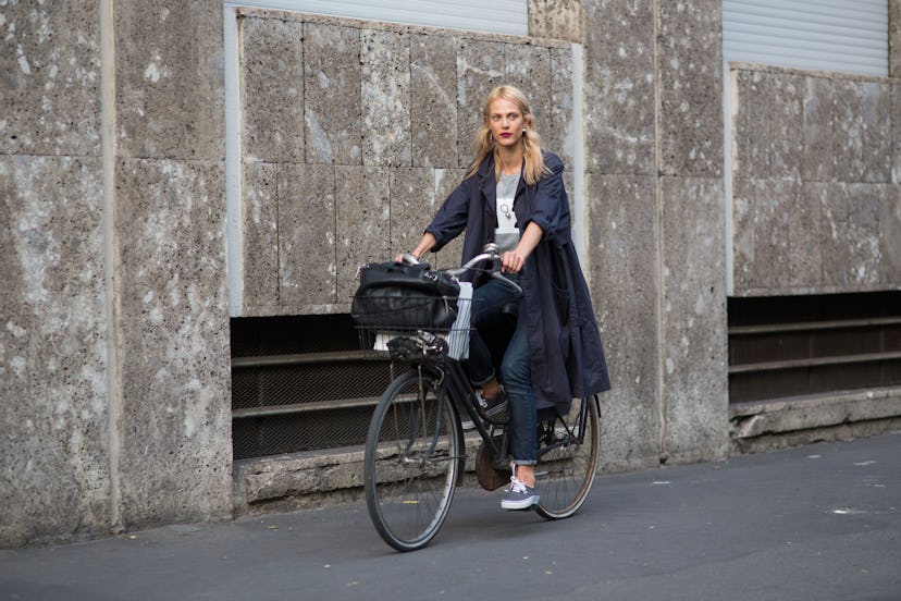Blonde girl wearing jeans, a gray t-shirt and a long navy raincoat while riding a street bike