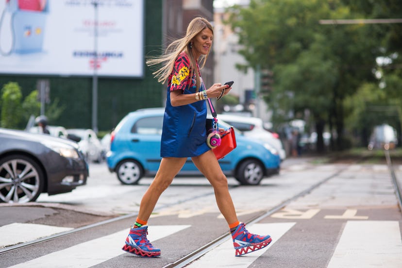 Woman crossing the road wearing a red patterned t-shirt under a short blue dress, red, blue and whit...