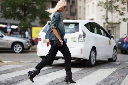 Blonde woman wearing a jeans jacket, black pants, and black boots crossing the street