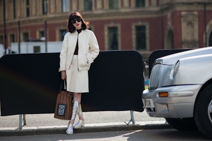 A woman with black hair wearing black sunglasses, a cream-colored coat, and a matching skirt 