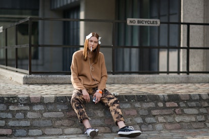 Lera Tribel sitting in a brown knit sweater, tie die pants, and black sneakers while holding a cigar...