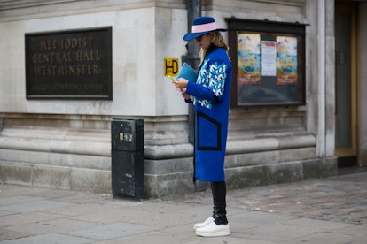 A woman texting on a street while wearing a blue coat with a rose-patterned blue hat, leather pants,...