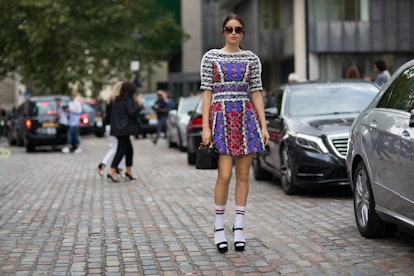 A woman wearing a short colorful dress, white striped sports socks, and black sandals while holding ...