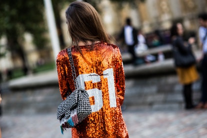 Girl posing in an orange sequined shirt with "61" on the back while holding a black & white purse