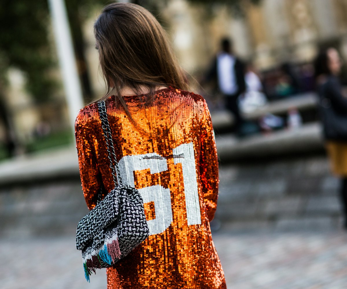 Girl wearing an orange sequined shirt with 61 on the back, and a black & white purse.