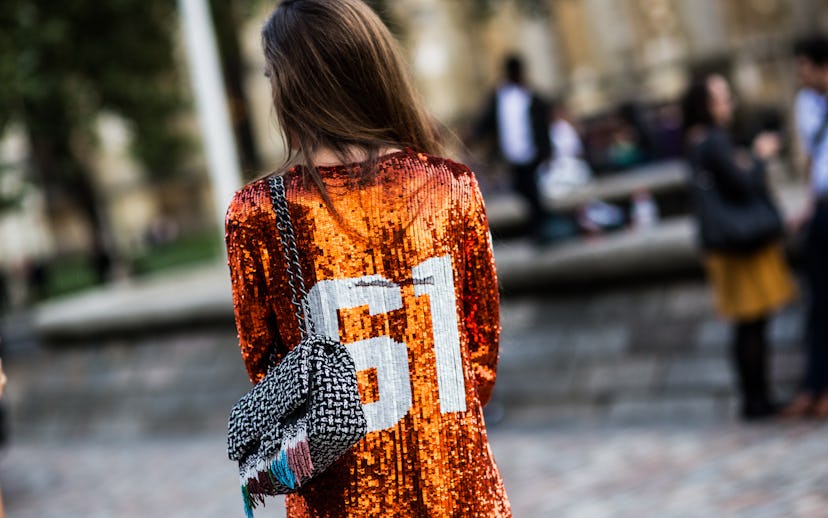 Girl wearing an orange sequined shirt with 61 number on the back, and a black & white purse