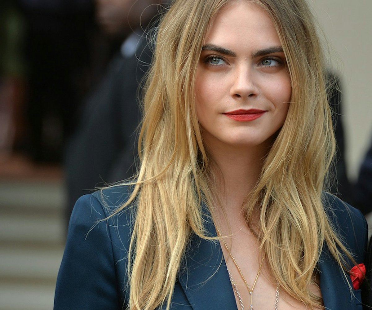 Cara Delevingne wearing red lipstick, and a messy hairstyle while giving a smug look 
