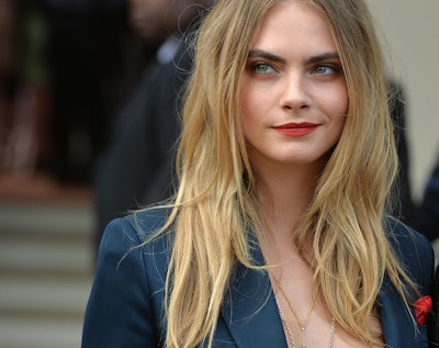 Cara Delevingne wearing red lipstick, and a messy hairstyle while giving a smug look 