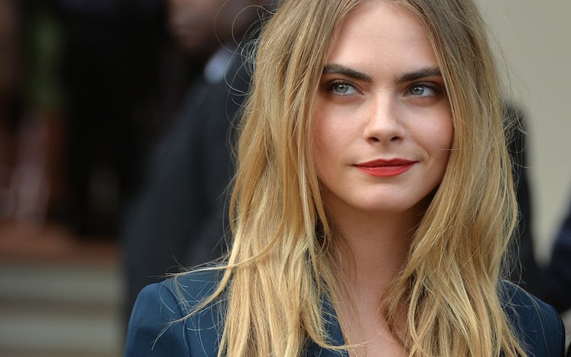 Cara Delevingne wearing red lipstick, and a messy hairstyle while giving a smug look  