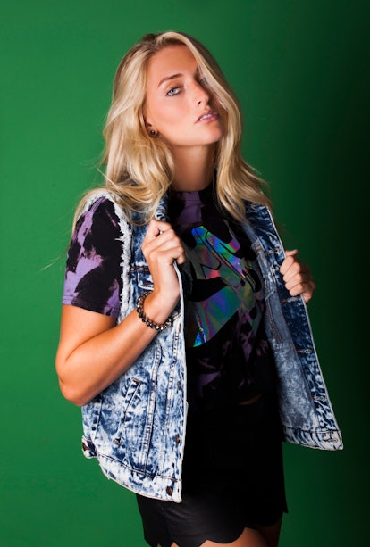 Blonde woman sporting a black shirt with blue and purple accents and a denim vest