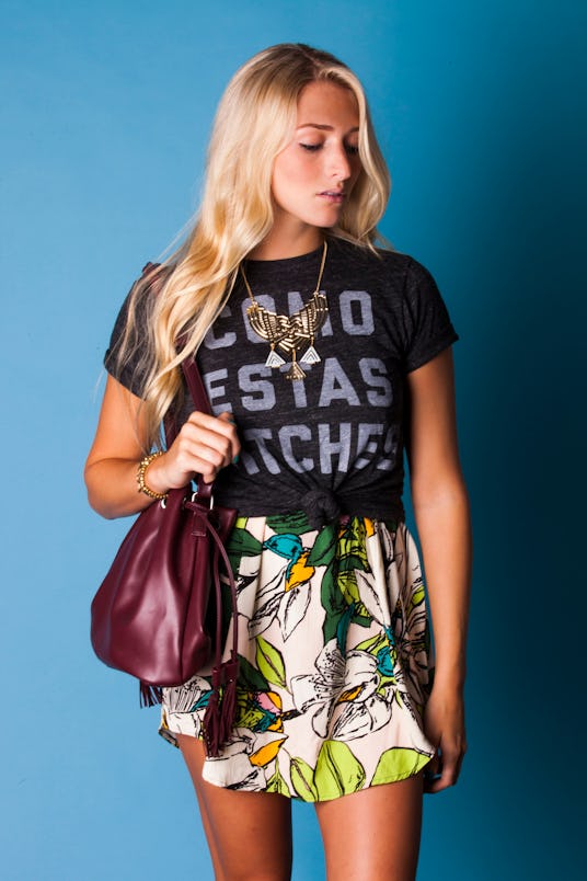 Blonde woman carrying a brown purse while sporting a graphic tee and a floral-patterned skirt lookin...