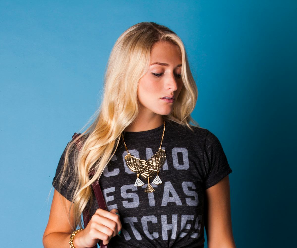 Blonde woman carrying a brown purse while sporting a graphic tee and a floral-patterned skirt.