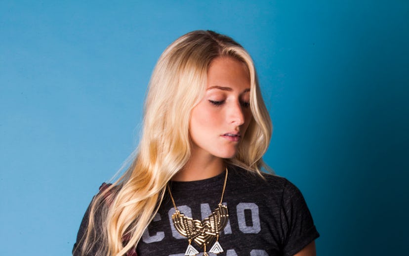 Blonde woman carrying a brown purse while sporting a graphic tee and a floral-patterned skirt.