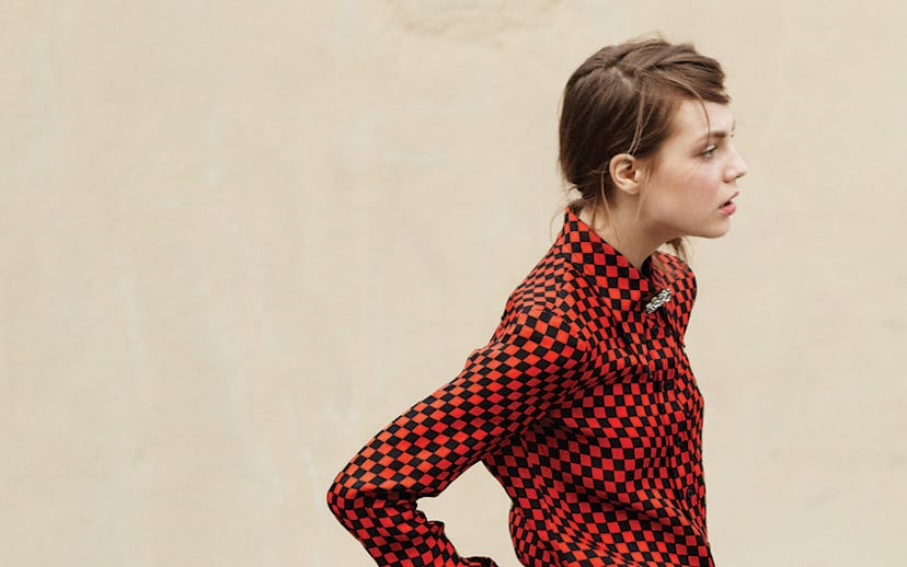 A model in a red checkered button-down shirt, colorful jeans, and black ankle boots