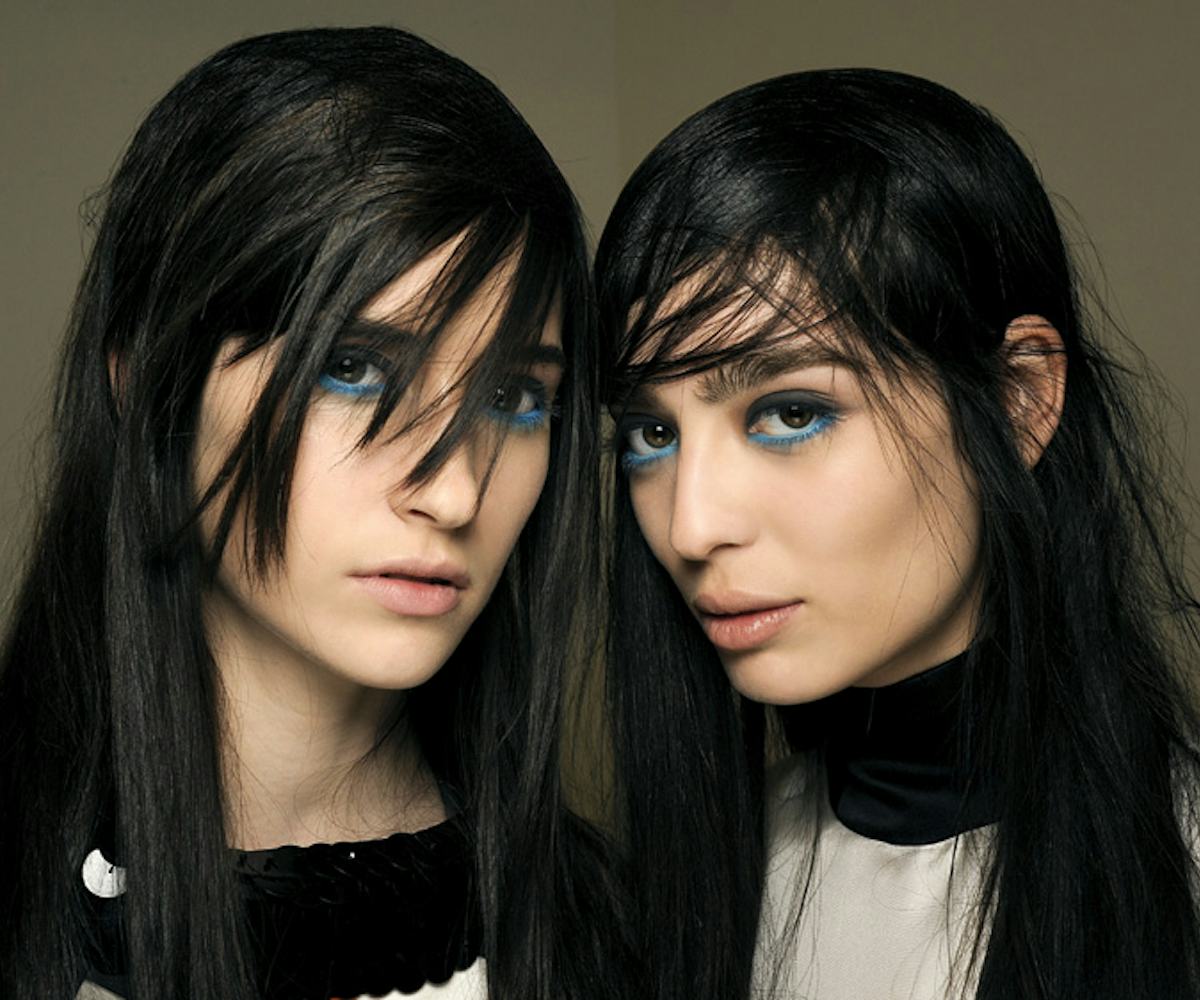 Two black-haired female models looking punk with teal-and-gray-rimmed eyes by makeup artist Lucia Pi...