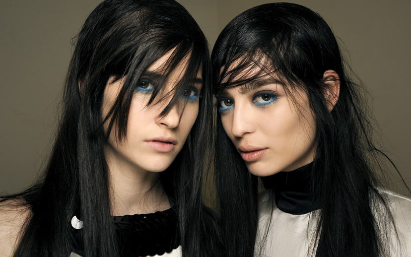 Two black-haired female models looking punk with teal-and-gray-rimmed eyes by makeup artist Lucia Pi...