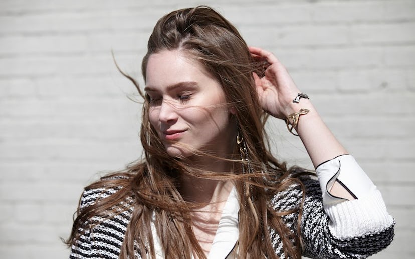 A brunette woman with closed eyes moving her hair away from her face