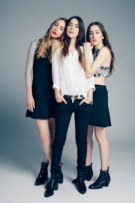 Danielle in a white blouse and black pants, Alana in a crop top and skirt, and Este in a long-sleeve...