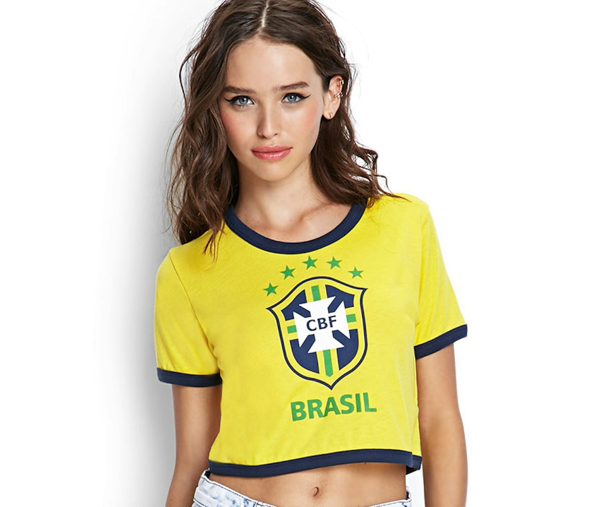 Model posing in denim shorts and in a yellow T-shirt with the "Brasil" soccer association logo