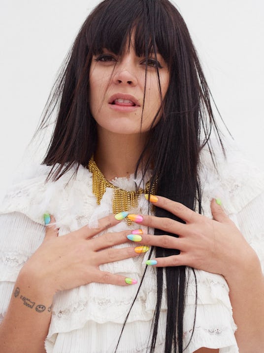 Lily Allen in a white ruffled shirt by Chanel and golden jewelry, with her hands on her chest 