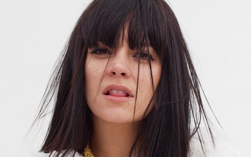 Lily Allen in a white shirt and golden-colored necklace holding her chest