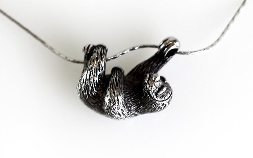 Silver necklace with little sloth attached to it, looking like he is climbing a branch