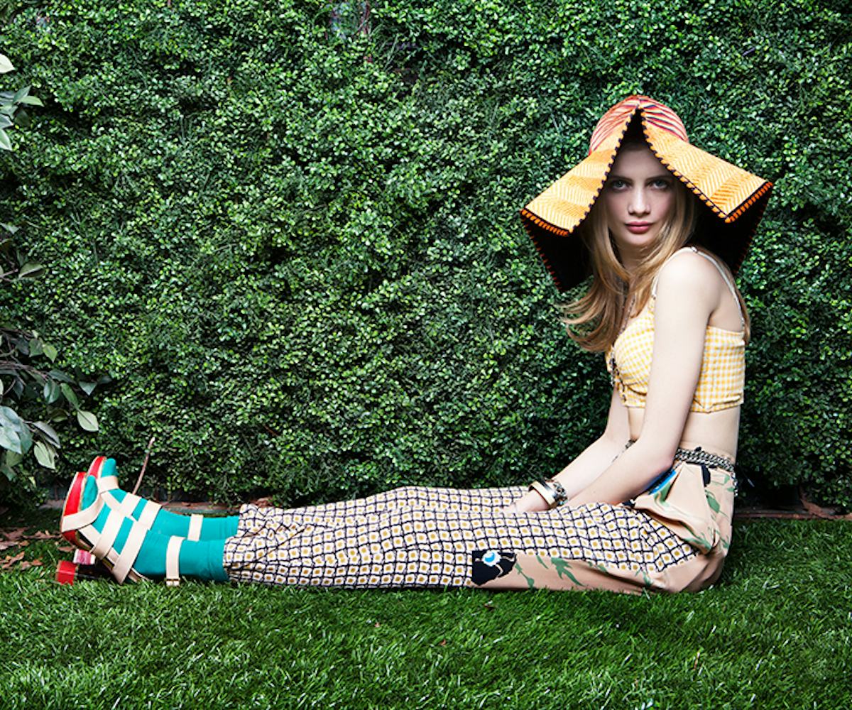 A fair-skinned girl sitting in grass with a big yellow straw hat on her head