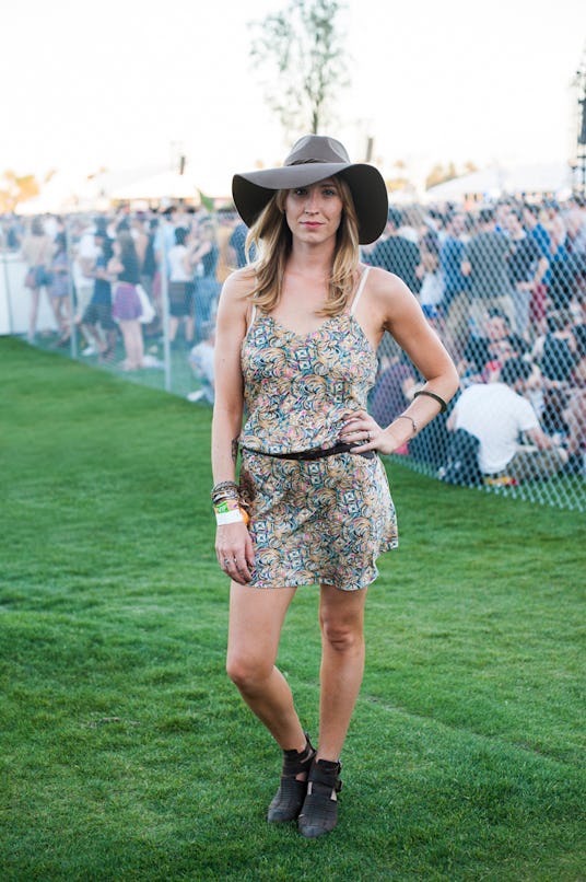 A woman in pastel green and beige floral dress with black belt, black cowboy hat, black boots, and b...