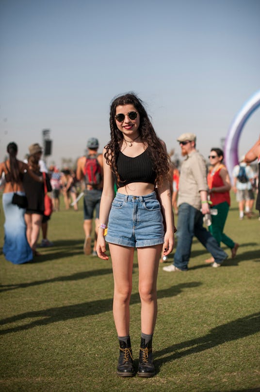 A woman in a short black top, high-waisted blue denim jeans and black boots with brown laces