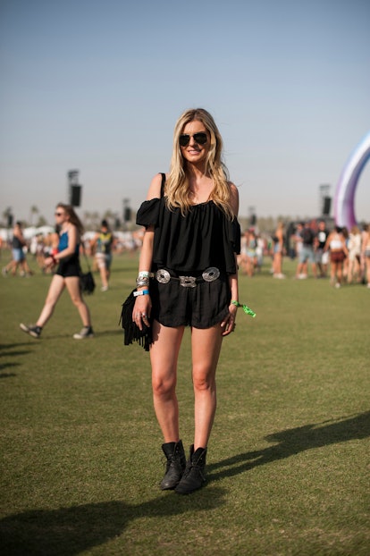 A woman in a black off-the-shoulder top and black shorts, black sunglasses and black ankle boots