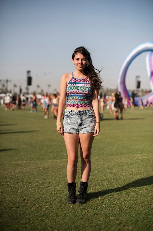 A woman with an Aztec print top and blue denim shorts, and black ankle boots
